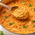 Creamy tomato orzo with chicken in a bowl, garnished with fresh herbs.