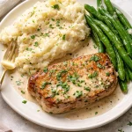 Creamy white wine pork chops with herbs and spices served on a plate.