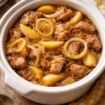 Slow cooker pork loin with sauerkraut and apples served in a rustic dish.