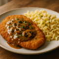 Breaded pork cutlet with mushroom sauce and buttered noodles on a white plate